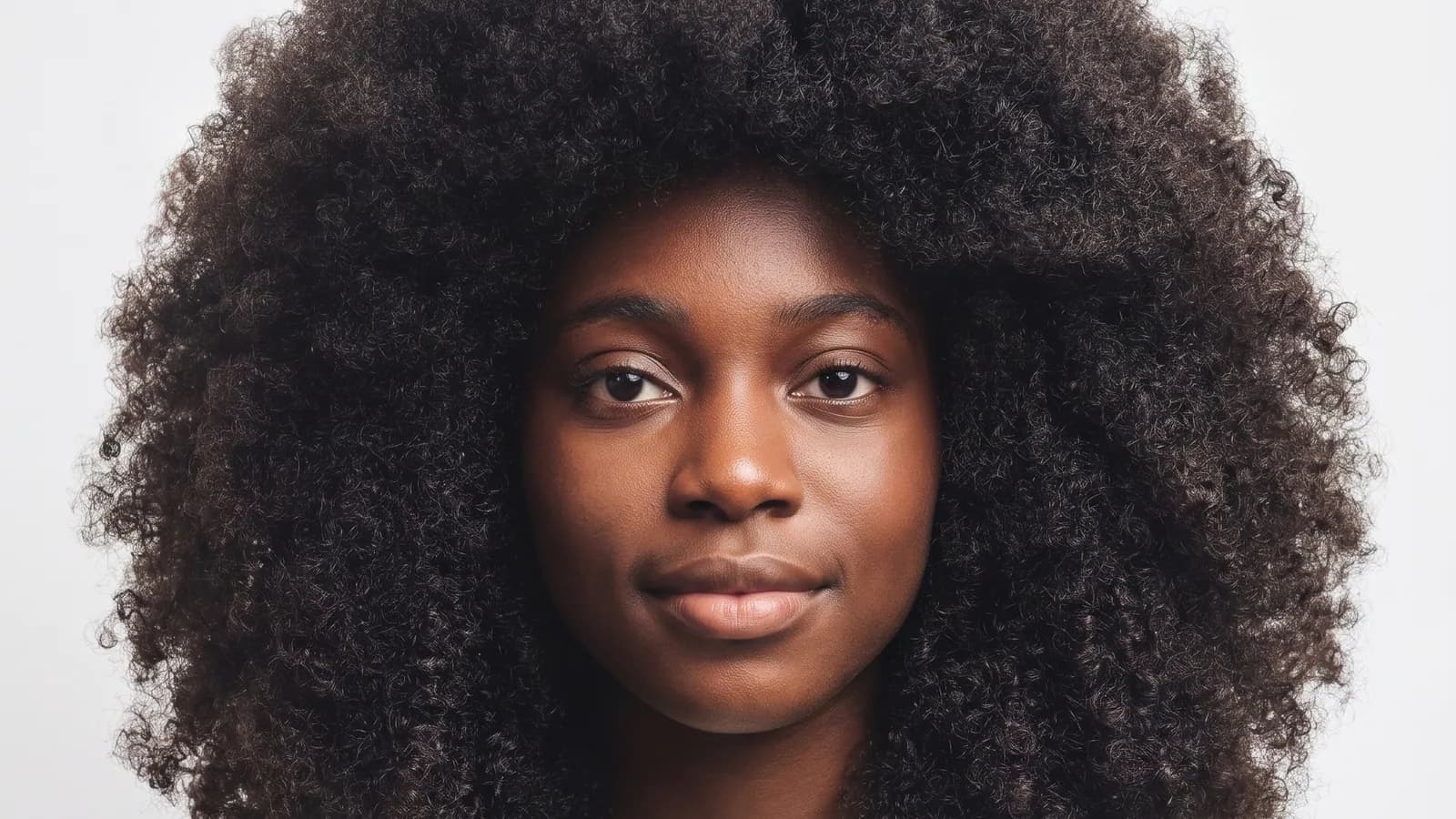 Portrait of a young woman with full, coily hair against a light background